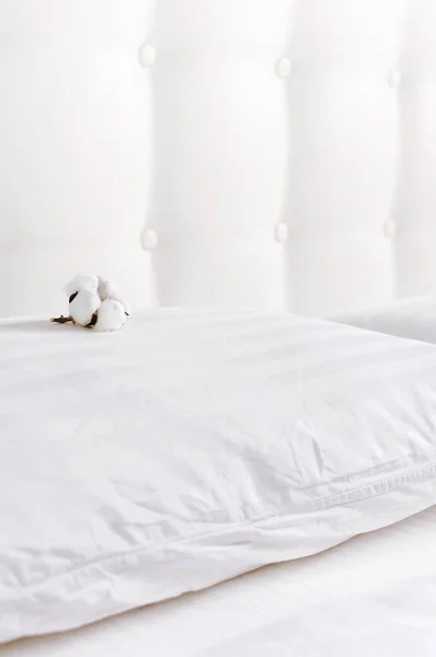 Софт белая стеганая подушка и хлопковый цветок в постели на фоне белой кожаной стеганой изголовья. Чистая подушка, часть кровати крупным планом, комфорт. Одеяло спинка спинки спинки кровати, макет кровати — стоковое фото