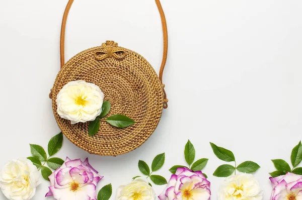 Concept à la mode de sacs à main pour femmes. Sac en rotin naturel bio fait à la main et délicates fleurs roses avec des feuilles vertes sur fond clair. Pose plate, Copier l'espace, vue du dessus. Ecobags de Bali . — Photo