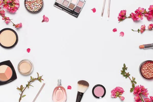 Different makeup cosmetic. Ball blush rouge face powder lipstick concealer bottle of perfume eyeshadow makeup brush spring pink flowers on light background top view flat lay. Beauty fashion background