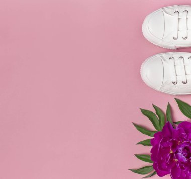 White female fashion sneakers and pink purple flowers peonies on pink background. Flat lay, top view, copy space. Women's shoes. Stylish white sneakers. Fashion blog or magazine concept.