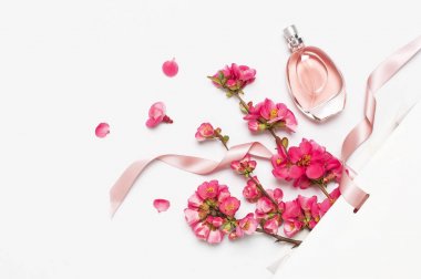 Şişe kadın parfüm ile pembe bahar çiçekler beyaz hediye paketi üzerinde ışık arka plan üst görünüm düz yatıyordu kopya alanı. Parfümeri kozmetik kadın aksesuarları koku koleksiyonu. Parfüm şişesi