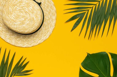 Kadın yaz hasır şapka, tropikal palmiye yaprakları, sarı arka planda Monstera yaprak üst görünümü düz kopya alanı yatıyordu. Yaz seyahati tatil konsepti. Kadın aksesuarı, yaz arka planı