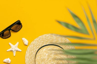 Kadınların hasır şapkası, tropikal palmiye yaprakları, canavar yaprağı, güneş gözlükleri, kabuklar, sarı arka planda deniz yıldızı düz zemin manzaralı fotokopi alanı. Yaz tatili konsepti. Kadın aksesuar, yaz.