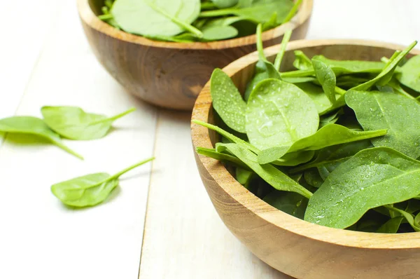 Fresh green spinach leaves on wooden bowl on white wooden rustic background top view copy space. Baby young spinach leaves, Ingredient for salad, healthy food, diet. Nutrition concept.