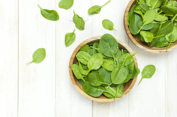 Fresh green spinach leaves on wooden bowl on white wooden rustic background top view copy space. Baby young spinach leaves, Ingredient for salad, healthy food, diet. Nutrition concept.
