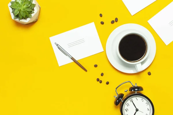 Flat lay taza de café negro, granos de café, reloj despertador negro, bolígrafos, tarjetas blancas, suculenta sobre fondo amarillo espacio de copia vista superior. Concepto creativo tiempo para trabajar, escritorio femenino, fondo de café —  Fotos de Stock