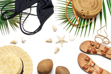 Kadının plaj aksesuarları düz yatıyordu. Yuvarlak trendy rattan çanta hasır şapka siyah mayo deri sandalet tropikal palmiye beyaz arka plan üzerinde hindistan cevizi deniz kabukları bırakır. En iyi görünüm kopyalama alanı. Yaz arka planı