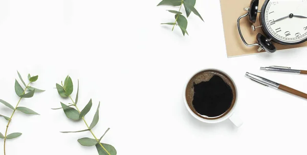 Plat gobelet de café noir, réveil noir, carnet, journal, eucalyptus sur fond blanc vue de dessus copier l'espace. Concept alimentaire minimaliste, espace de travail de bureau féminin, temps de travail fond de café — Photo