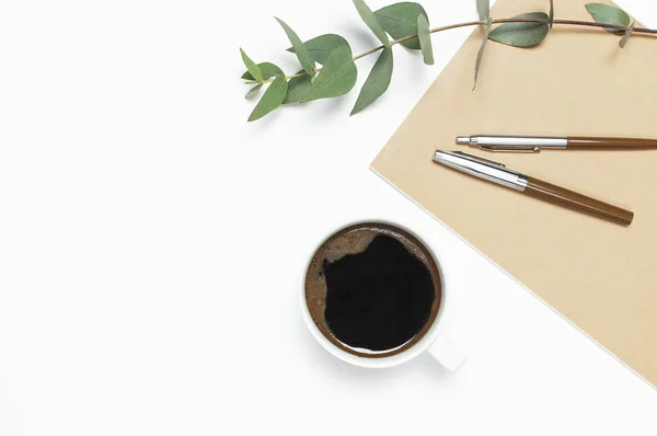 Kopje zwarte koffie, notebook, dagboek, pennen, groene takje van eucalyptus op witte achtergrond. Platte lay, bovenaanzicht, kopieer ruimte. Vrouwelijk bureau werkplek, ochtend ontbijt, warme drank, koffie achtergrond — Stockfoto