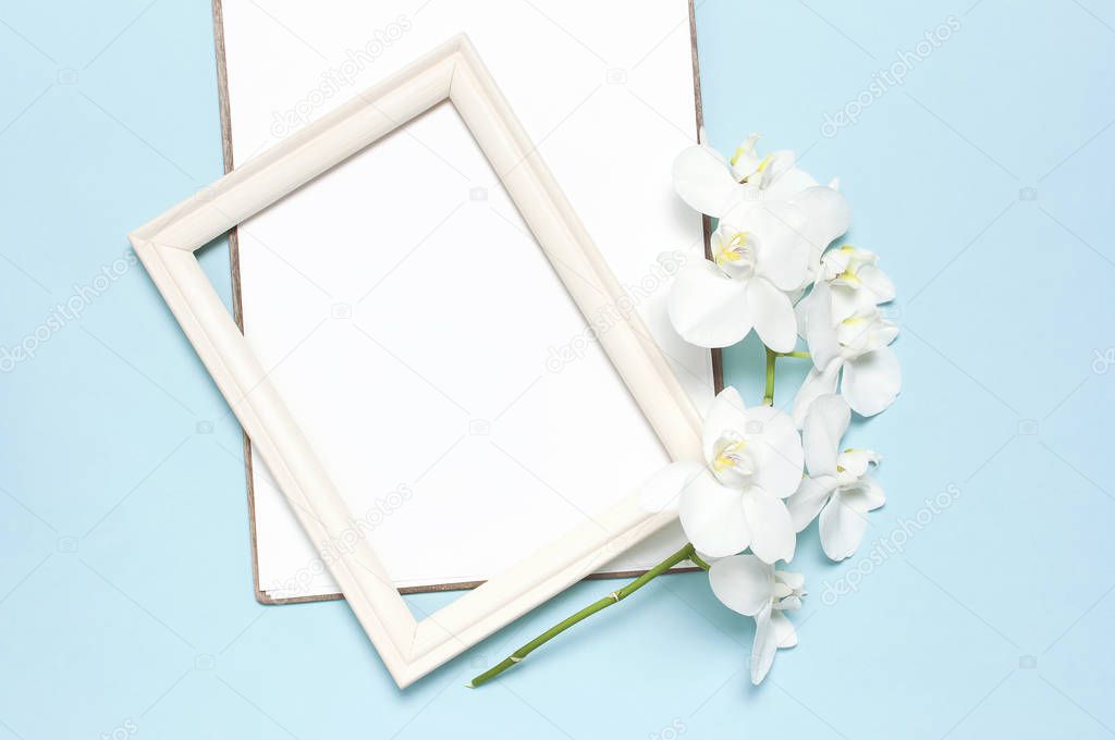 Beautiful White Phalaenopsis orchid flowers, wooden white photo frames on blue background top view flat lay. Tropical flower, branch of orchid close up. Orchid background. Women's Day, Flower Card