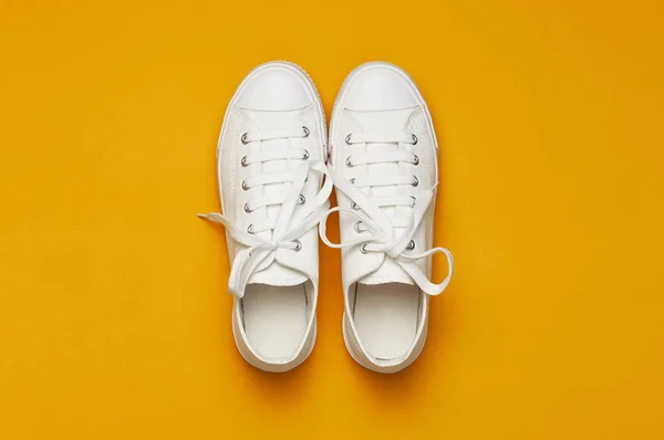 Sarı turuncu arka plan üzerinde beyaz kadın moda spor ayakkabıları. Düz lay üst görünüm kopyalama alanı. Kadın ayakkabıları. Şık beyaz spor ayakkabılar. Moda blog veya dergi kavramı. Minimalist ayakkabı arka plan, spor — Stok fotoğraf