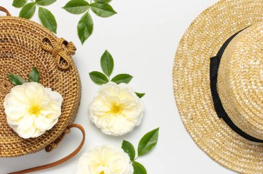 Kadın çanta moda kavramı. El yapımı doğal organik rattan çanta, hasır şapka, hafif arka plan üzerinde yeşil yaprakları ile narin gül çiçekleri. Düz yatıyordu, Kopyalama alanı, üst görünüm. Bali gelen Ecobags.