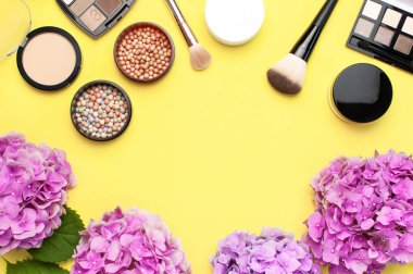 Set dekoratif kozmetik maskara tozu ruj göz farı allık makyaj fırçası pembe ortanca çiçekler sarı arka plan üst görünümü Düz yatıyordu kopya alanı. Güzellik blogger kavramı. Moda arka plan