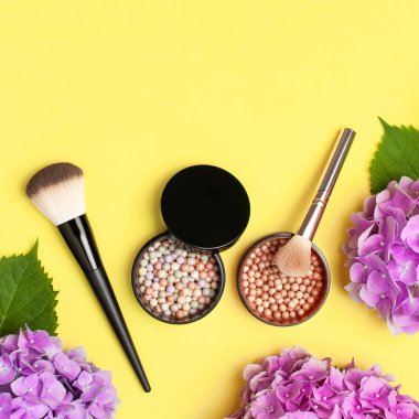 Dekoratif kozmetik makyaj fırçaları seti, allık yüz topları, sarı arka plan üst görünümü Düz üzerinde pembe ortanca çiçekler kopya alanı yatıyordu. Güzellik blogger kavramı. Moda geçmişi. Makyaj aksesuarları