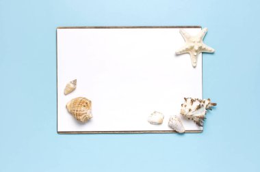 Yaz konsepti, deniz geçmişi. Deniz kabukları, denizyıldızı, pastel mavi arka plan üzerine beyaz boş çarşaf. Üst görünüm, düz döşeme, kopyalama alanı. Deniz yaz tatili Mockup. Seyahat, deniz hatırası.