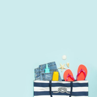 Yaz deniz aksesuarları. Plaj çantası Coral flip flop denim şort kabukları denizyıldızı güneş kremi şişe vücut spreyi mavi arka plan üst görünümü düz yatıyordu. Yaz geçmişi. Tatil tatil seyahat konsepti