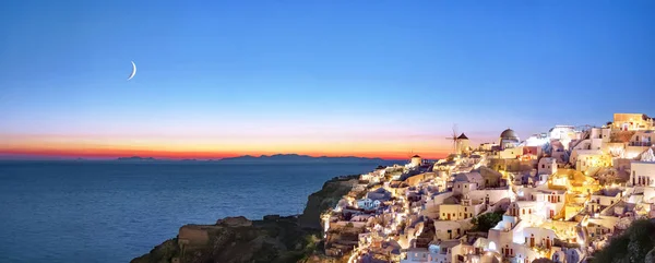 Oia ao pôr-do-sol. Bela vista panorâmica da aldeia de Oia, Santorini, Grécia, mar Egeu, Europa. Arquitetura grega branca clássica, casas, igrejas, moinhos de vento. Vista noturna, lua no céu — Fotografia de Stock