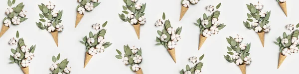 Pattern from waffle cone with bouquet of cotton flowers and fresh eucalyptus twigs on light gray background. Creative Delicate white cotton flowers minimal concept. Flat lay top view copy space — Stock Photo, Image