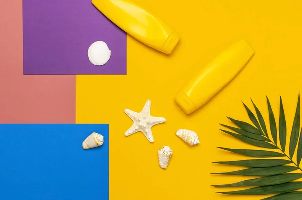 Yellow bottles of sunscreen cream, tropical palm leaves, shells, starfish on colorful background top view flat lay copy space. Sun protection. Summer background, vacation, travel concept