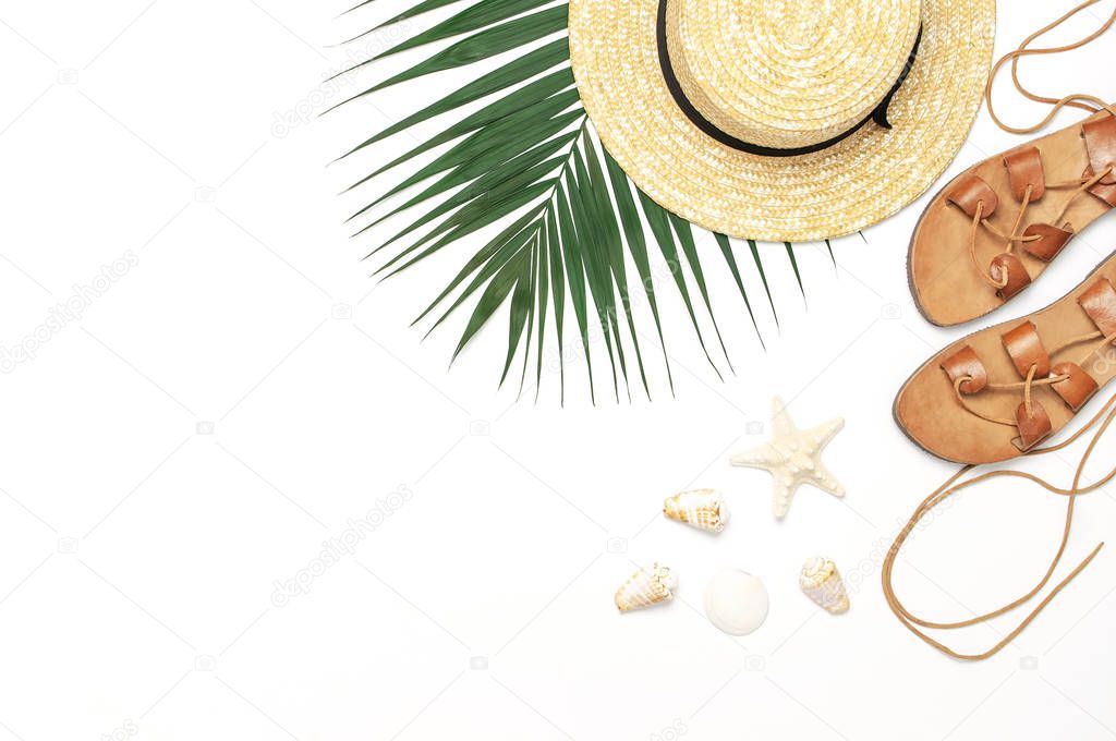 Woman's beach accessories flat lay. Straw hat, leather sandals, tropical palm leaves, seashells, starfish on white background. Top view copy space. Summer backdrop