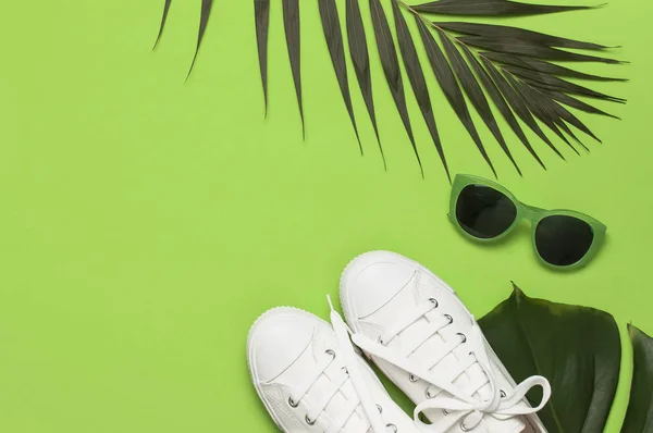 Białe damskie sneakers mody, modne okulary przeciwsłoneczne, tropikalne liście na zielonym tle. Płaski lay góry widok przestrzeni kopiowania. Obuwie damskie, akcesoria. Stylowe, białe tenisówki. Kreatywna letnia koncepcja — Zdjęcie stockowe