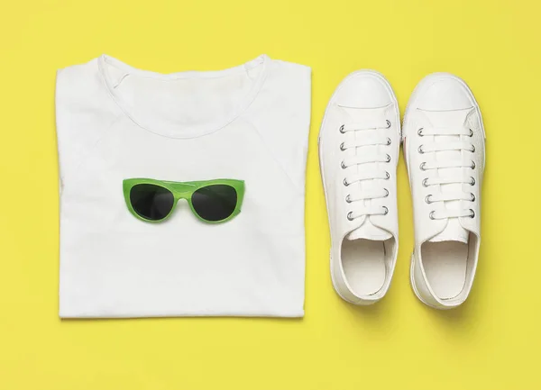 Λευκά γυναικεία παπούτσια μόδας, μοντέρνα γυαλιά ηλίου, λευκό μπλουζάκι σε κίτρινο φόντο. Επίπεδη όψη αντίγραφο χώρου αντιγραφής. Γυναικεία παπούτσια, αξεσουάρ. Κομψά λευκά αθλητικά παπούτσια. Δημιουργική ιδέα μόδα blog — Φωτογραφία Αρχείου