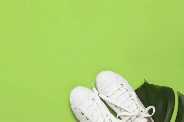 Bílé ženské módní tenisky, tropické listí na zeleném pozadí. Plochá plocha pro kopírování zobrazení nahoře. Dámské boty, doplňky. Stylové bílé tenisky. Kreativní letní koncepce — Stock fotografie