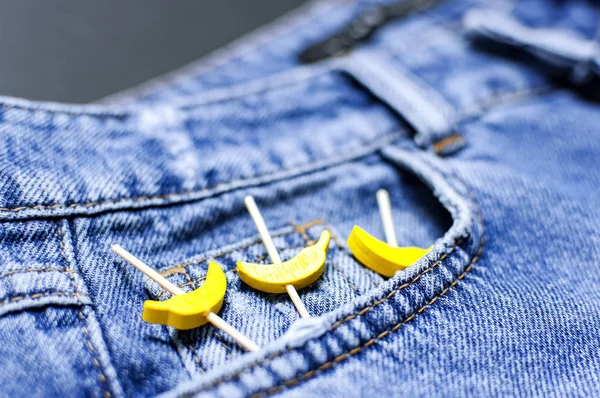 Blue jeans and yellow wooden bananas from a pocket on black background top view flat lay. Detail of nice blue jeans. Jeans texture or denim background. Trend clothing. Fashion, Selective focus — Stock Photo, Image