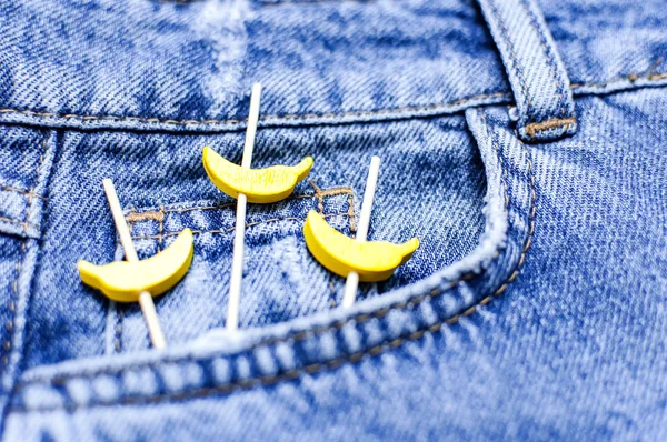 Niebieskie dżinsy i żółte drewniane banany z kieszeni na czarnym tle góry widok płaski lay. Szczegóły ładne niebieskie dżinsy. Dżinsy tekstury lub denim tle. Odzież trend. Moda, selektywna ostrość — Zdjęcie stockowe