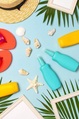 Yaz moda düz yatıyordu. Hasır şapka mercan parmak arası terlik tropikal palmiye yaprakları güneş kremi beyaz fotoğraf çerçevesi hindistan cevizi deniz kabukları mavi arka plan üzerinde denizyıldızı. En iyi görünüm kopyalama alanı. Yaratıcı tatil arka planı