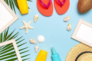 Yaz moda düz yatıyordu. Hasır şapka mercan parmak arası terlik tropikal palmiye yaprakları güneş kremi beyaz fotoğraf çerçevesi hindistan cevizi deniz kabukları mavi arka plan üzerinde denizyıldızı. En iyi görünüm kopyalama alanı. Yaratıcı tatil arka planı