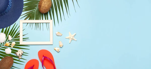 Summer fashion flat lay. Blue hat coral flip flops tropical palm leaves sunscreen white photo frame coconut seashells starfish on blue background. Top view copy space. Creative vacation background