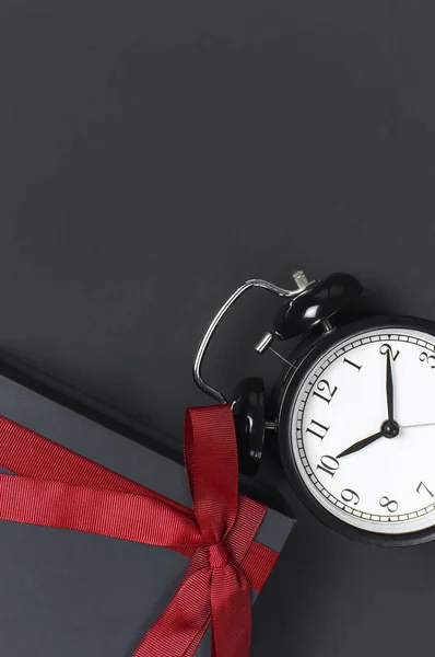 Black retro alarm clock and gift box with red ribbon on gray dark background top view Flat lay copy space. Minimalistic background, concept of time, celebration, congratulation time — Stock Photo, Image