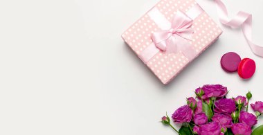 Açık gri arka planda şerit, parlak pembe güller, kek Macaron veya acıbadem kurabiyesi ile hediye kutusu. Düz yatıyordu, üst görünüm, kopya alanı. Doğum günü, kadın veya anneler günü için tebrik kartı. Çiçekler kompozisyon