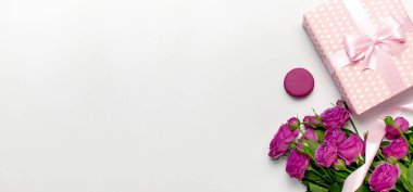 Açık gri arka planda şerit, parlak pembe güller, kek Macaron veya acıbadem kurabiyesi ile hediye kutusu. Düz yatıyordu, üst görünüm, kopya alanı. Doğum günü, kadın veya anneler günü için tebrik kartı. Çiçekler kompozisyon
