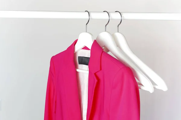 Chaqueta de mujer de color rosa brillante en percha de madera blanca en la barra contra la pared gris claro espacio de copia laico plano. Chaqueta de moda, ropa de tendencia femenina, fondo de moda. Concepto de tienda, venta —  Fotos de Stock