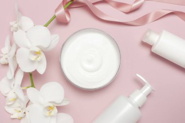 Güzellik Spa konsepti. Krem ile açılan konteyner, kozmetik şişe kapları, pembe arka plan Düz üzerinde beyaz Phalaenopsis orkide çiçekleri üst görünümü yatıyordu. Bitkisel dermatoloji kozmetik hijyenik krem