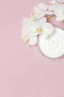Güzellik Spa kavramı. Krem ve pembe bir arka plan düz beyaz Phalaenopsis orkide çiçekler ile açılan plastik konteyner üstten görünüm yatıyordu. Bitkisel Dermatoloji kozmetik hijyenik krem, organik kozmetik doğal