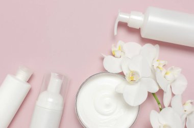 Güzellik Spa konsepti. Krem ile açılan konteyner, kozmetik şişe kapları, pembe arka plan Düz üzerinde beyaz Phalaenopsis orkide çiçekleri üst görünümü yatıyordu. Bitkisel dermatoloji kozmetik hijyenik krem