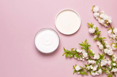 Güzellik Spa konsepti. Pembe arka plan Düz üzerinde krem ve bahar Beyaz çiçekler ile açılan plastik konteyner üst görünümü yatıyordu. Bitkisel dermatoloji kozmetik hijyenik krem, organik kozmetik Doğal