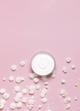 Güzellik Spa konsepti. Pembe arka plan Düz üzerinde krem ve bahar Beyaz çiçekler ile açılan plastik konteyner üst görünümü yatıyordu. Bitkisel dermatoloji kozmetik hijyenik krem, organik kozmetik Doğal
