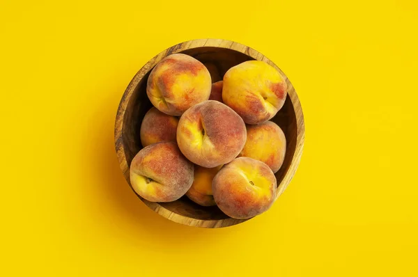 Плоска композиція з персиками. Стиглі соковиті персики в дерев'яній мисці на жовтому тлі. Плоский простір, вид зверху, простір для копіювання. Свіжі органічні фрукти, веганська їжа. Концепція врожаю — стокове фото