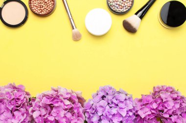 Dekoratif kozmetik makyaj fırçaları seti, allık yüz topları, sarı arka plan üst görünümü Düz üzerinde pembe ortanca çiçekler kopya alanı yatıyordu. Güzellik blogger kavramı. Moda geçmişi. Makyaj aksesuarları