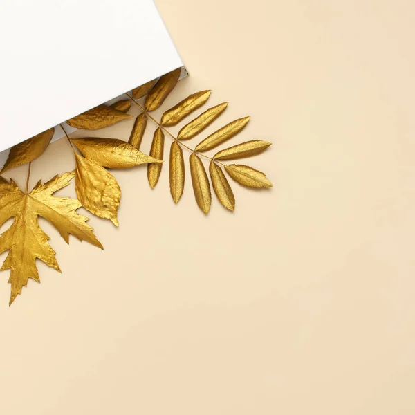 Flach lag kreative Herbstkomposition. weiße Geschenkpapier-Paket und goldene Blätter auf beigem Hintergrund Draufsicht Kopierraum. Herbstkonzept. Herbsthintergrund. Minimale Konzeptidee, florales Design — Stockfoto