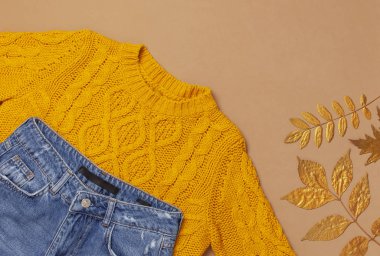 Sonbahar Moda Konsepti. Kadın turuncu örme kazak pullover, mavi kot pantolon, kahverengi arka plan üst görünüm düz üzerinde altın sonbahar yaprağı kopyalama alanı yatıyordu. Modaya uygun kadın aksesuarları. Şık Bayan Giyim