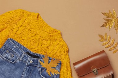 Sonbahar Moda Konsepti. Kahverengi deri kadın çanta, turuncu örme kazak, mavi kot pantolon, kahverengi arka plan üst görünüm düz düz üzerinde altın sonbahar yaprağı kopyalama alanı yatıyordu. Moda kadın aksesuarları Kadın Giyim