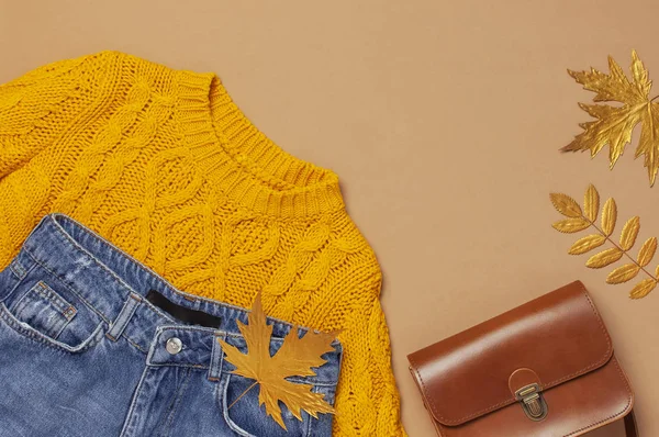 Φθινοπωρινό σχέδιο μόδας. Καφέ δερμάτινη γυναίκα τσάντα, πορτοκαλί πλεκτό πουλόβερ, μπλε τζιν, χρυσή όψη του φθινοπώρου σε καφέ φόντο επάνω θέα επίπεδη θέση θέσει αντίγραφο χώρου. Μοντέρνα γυναικεία αξεσουάρ γυναικεία ρούχα — Φωτογραφία Αρχείου