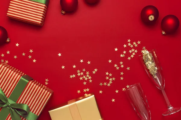 Yeni Yıl Noel hediyeleri, Noel topları, şampanya bardakları, kırmızı arka plan üst görünümünde altın konfeti yıldız. Düz xmas tatil 2020 kutlama yatıyordu. Hediye kutuları tebrik kartı Şenlikli süslemeleri