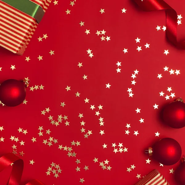 Nowy rok prezenty świąteczne z zieloną wstążką, Boże Narodzenie kulki, Złote konfetti gwiazdki na czerwonym tle widok z góry. Płaski lay Xmas święto 2020 uroczystości. Pudełka upominkowe karty okolicznościowe Dekoracje świąteczne — Zdjęcie stockowe