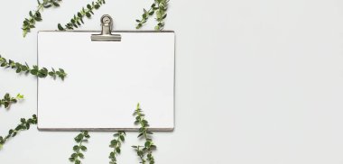 Klasör ve metal clothespin ile boş beyaz kağıt, gri arka plan üst görünüm düz üzerinde bitkilerin bahar yeşil dalları kopyalama alanı yatıyordu. Dekoratif bitki dalı, çiçek kompozisyon mockup Minimalist tarzı